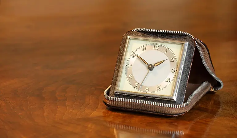 Eine klassische Vintage-Reiseuhr in einem Lederetui auf einem Holztisch als Symbol für Zeitmanagement und effiziente Methoden für Erfolg